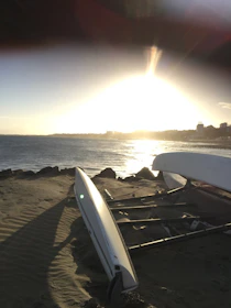 Sunset casting golden light over kayaks resting on a sandy beach with gentle waves lapping nearby.