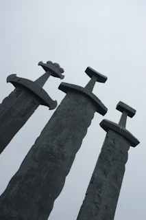 A detailed illustration of the Five of Swords tarot card showing a figure holding three swords with two defeated figures in the background under a cloudy sky.