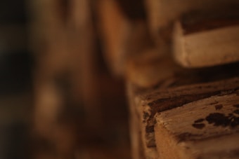 A close-up view of stacked wooden planks, highlighting the texture and grain of the wood. The planks have a worn and rustic appearance, with varying shades of brown and visible knots.