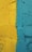 A textured wall featuring two bold colors, with a distinct dividing line separating a vibrant yellow from a striking teal. The wall's surface has a rough, uneven texture, adding depth to the color contrast.