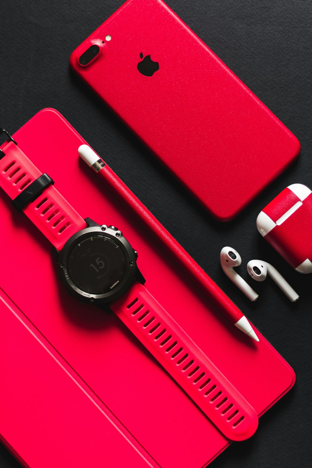 Smartwatch, Stylus, AirPods und Produkt rotes iPhone 7 auf schwarzer Oberfläche