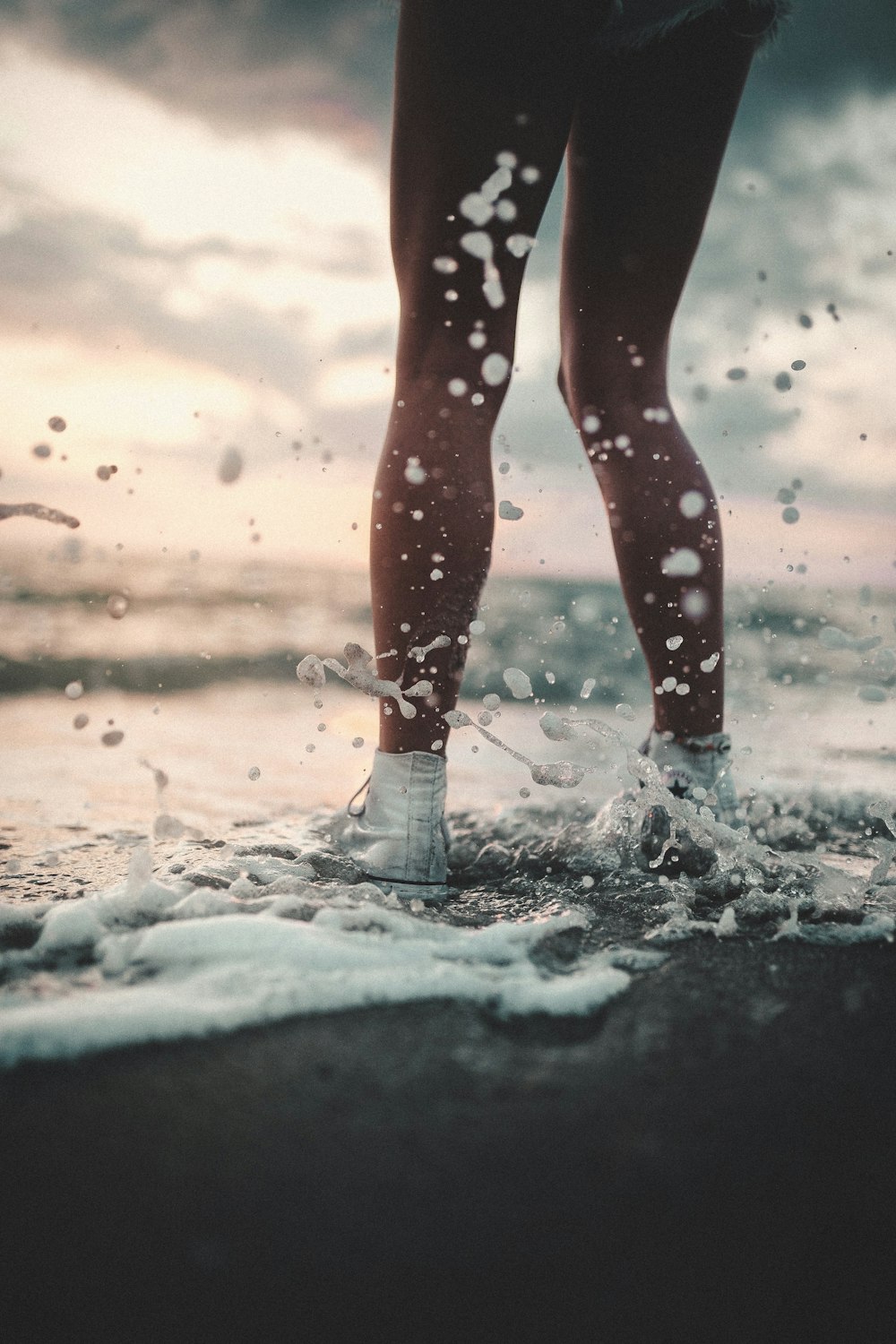 person wearing high-top sneaker playing sea waves on seashore