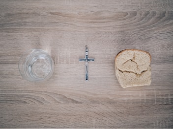 closeup photo of silver-colored cross pendant beside baked bread