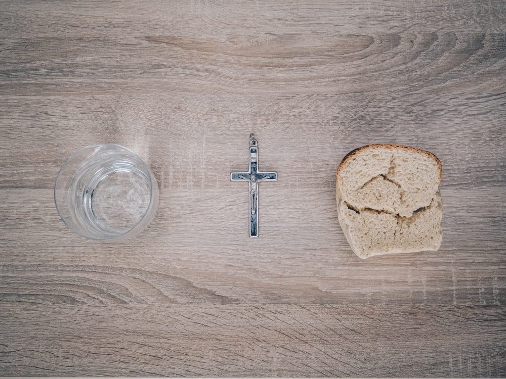 closeup photo of silver-colored cross pendant beside baked bread