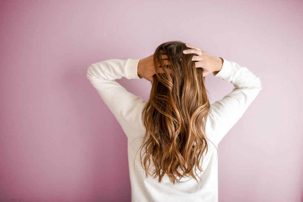 Donna in camicia bianca a maniche lunghe in piedi davanti al muro rosa