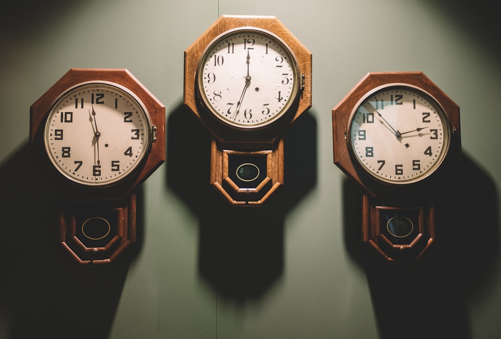 three brown framed white analog wall clocks hanging by wall