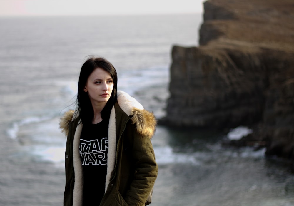 woman in brown parka jacket standing on rock formation