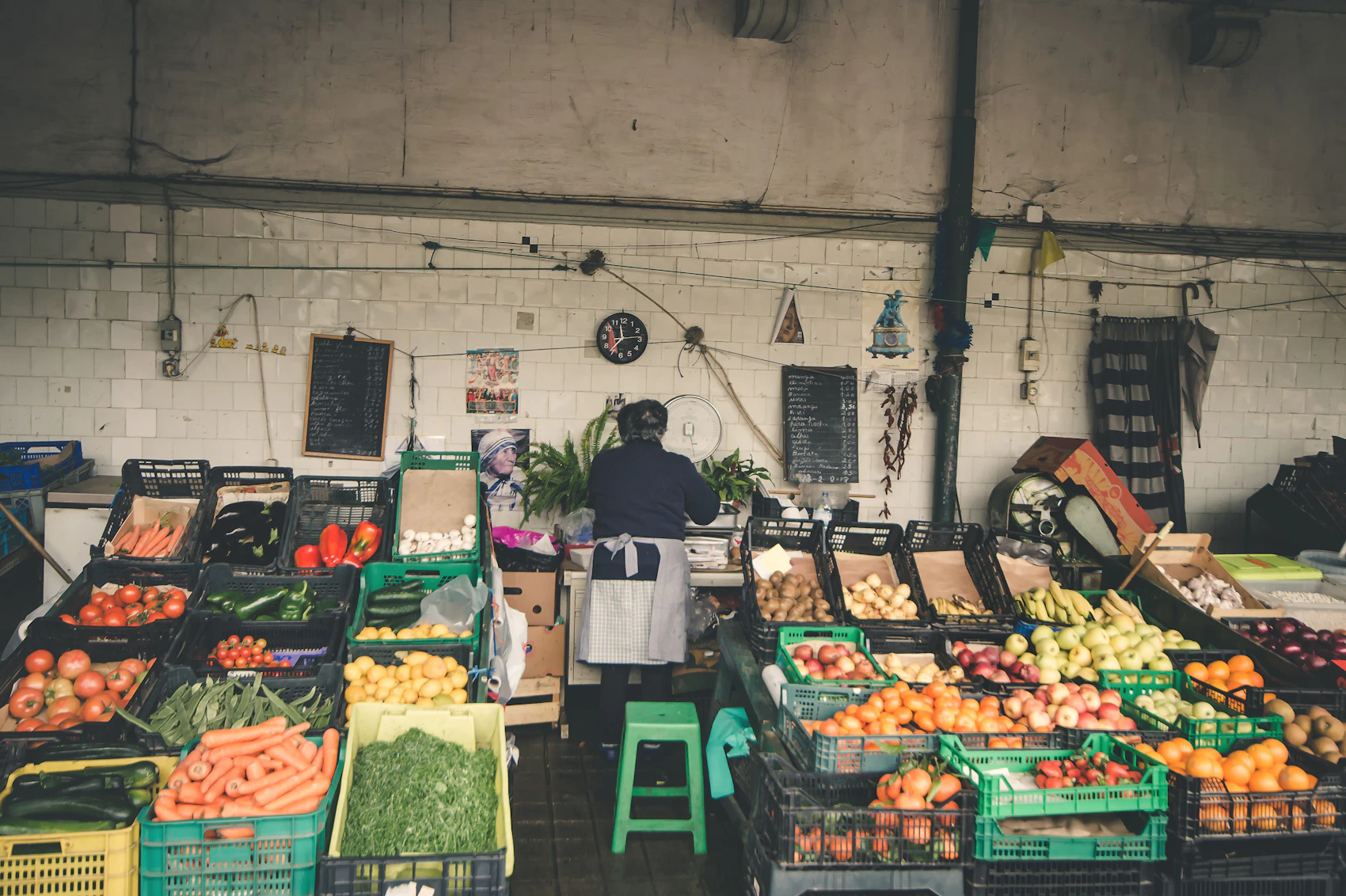 A produce seller surrounded by colourful fruit and vegetables at Bolhão Market in Porto