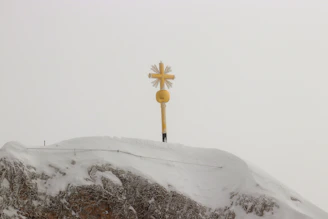 A golden cross silhouetted against a sunrise over a quiet mountain path.