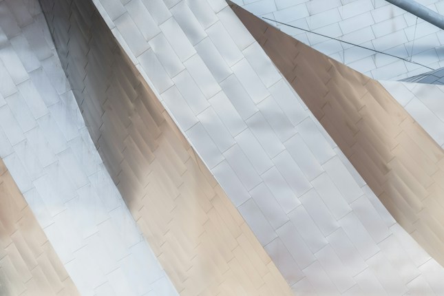 A close-up view of architectural elements featuring intersecting panels with a smooth metallic texture. The panels are arranged in a geometric pattern, creating a sense of depth and modernity.