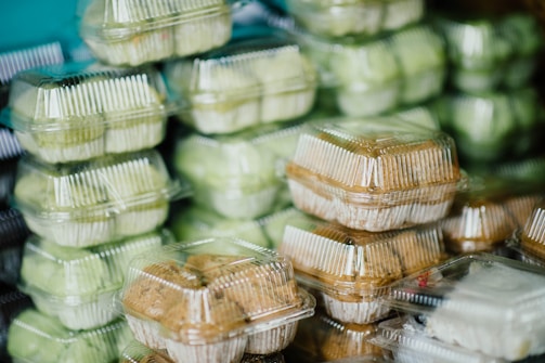 Several stacks of clear plastic containers filled with food items, with some of the containers holding light green items and others holding brown baked goods.