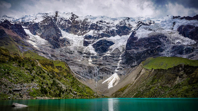 A turquoise glacial lake beneath a snow-capped peak in the Cusco region of Peru