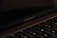 A close-up view of a MacBook Pro laptop screen and keyboard. The focus is on the MacBook Pro label below the screen, with the keyboard keys visible in the foreground. The lighting is low and the atmosphere is subdued, lending a sleek and minimalistic feel.