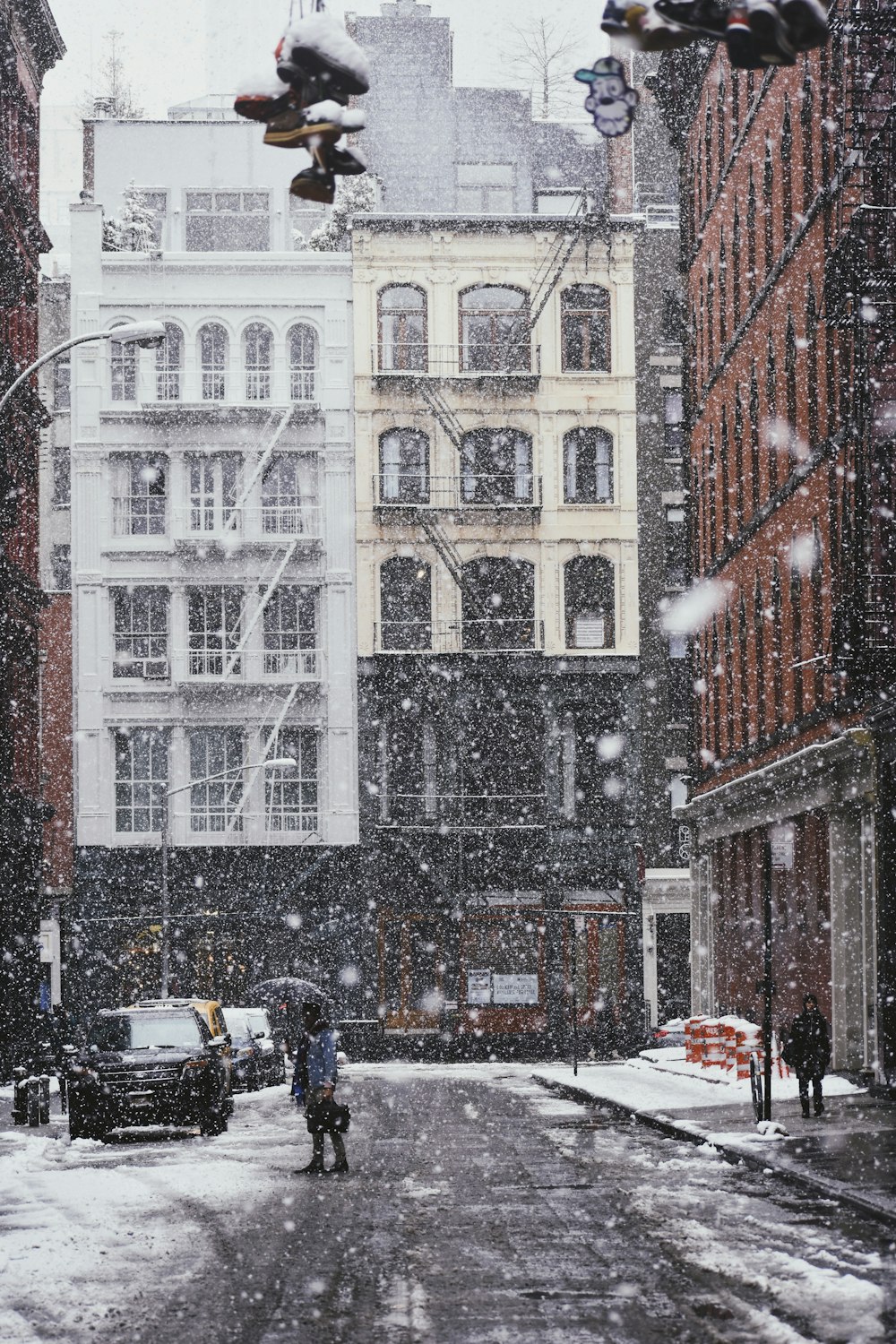 persona sotto ombrello nero in piedi sulla strada asfaltata grigia coperta di neve vicino all'edificio commerciale e alle automobili durante il giorno