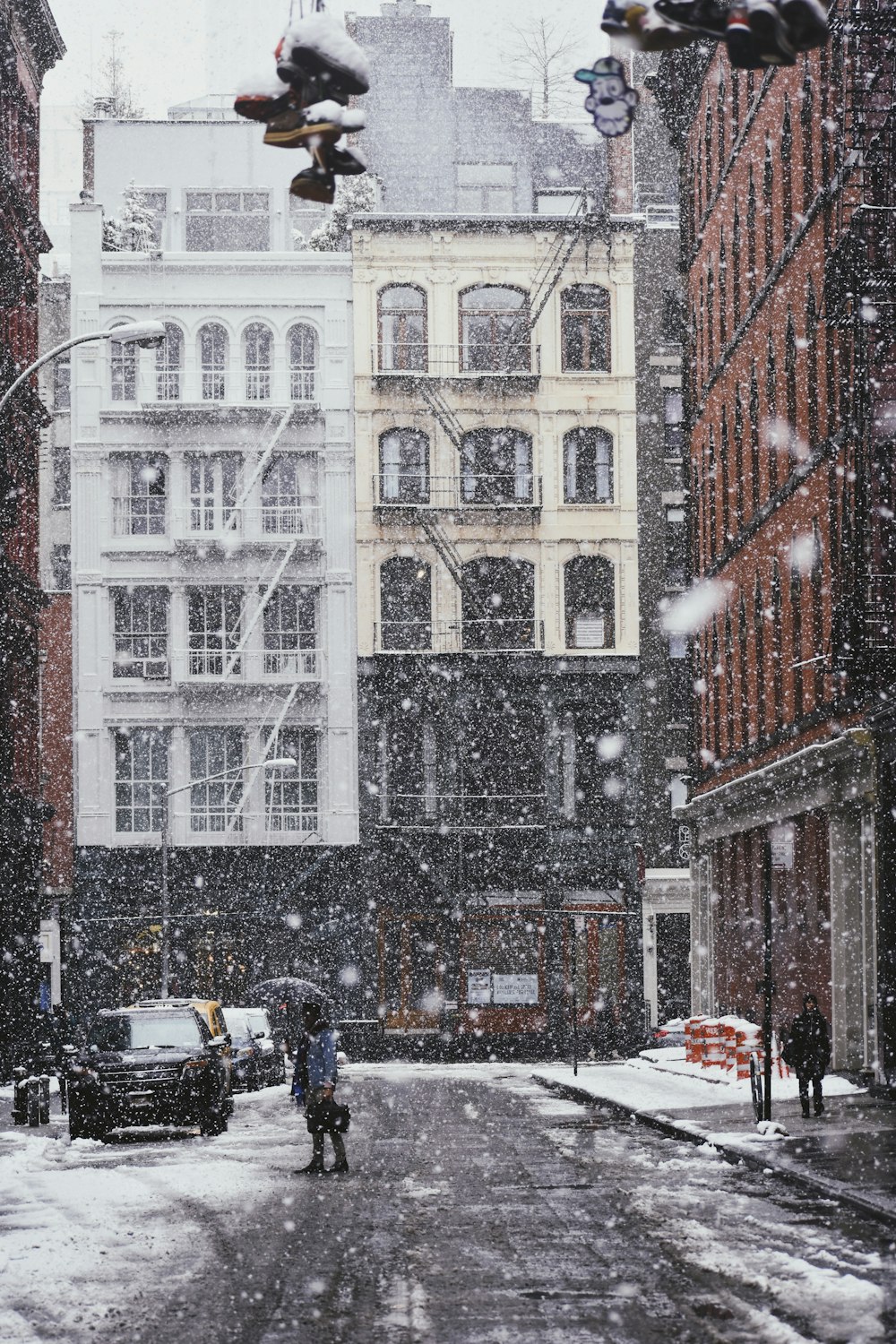 person under black umbrella standing on gray asphalt road covered with snow near commercial building and cars during daytime