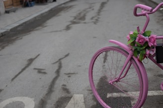 A pink bag hanging on a bicycle handlebar in a sunny street.