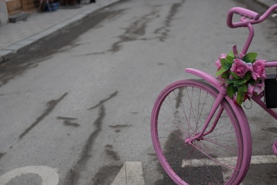 A pink bag hanging on a bicycle handlebar in a sunny street.