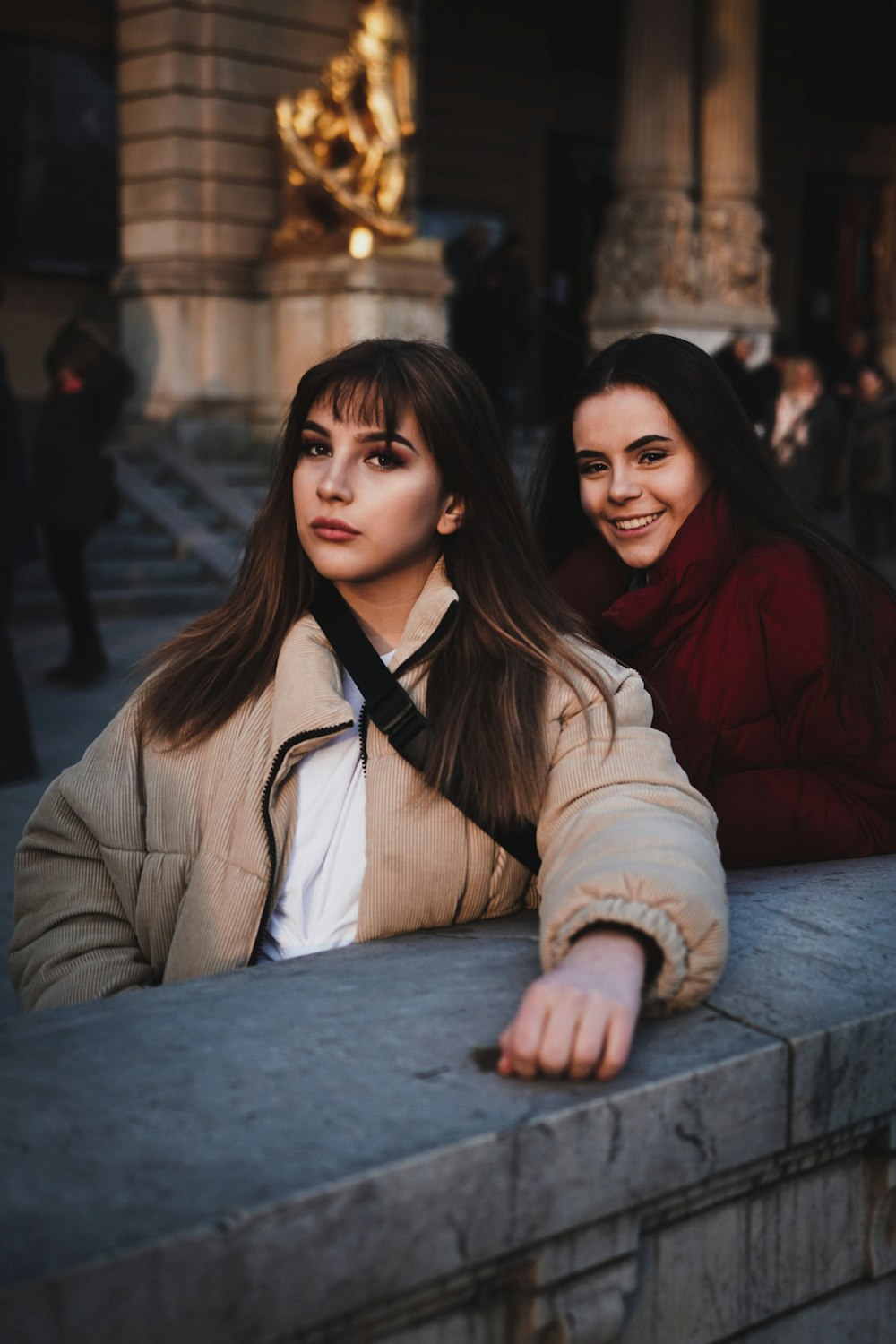 two women leaning on gray wall