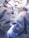 Two surgeons wearing blue surgical gowns and caps perform an operation under bright surgical lights. Medical equipment and monitors surround them in a sterile operating room environment.