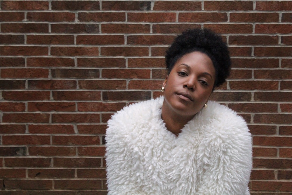 woman in white fur coat in front of the brick wall