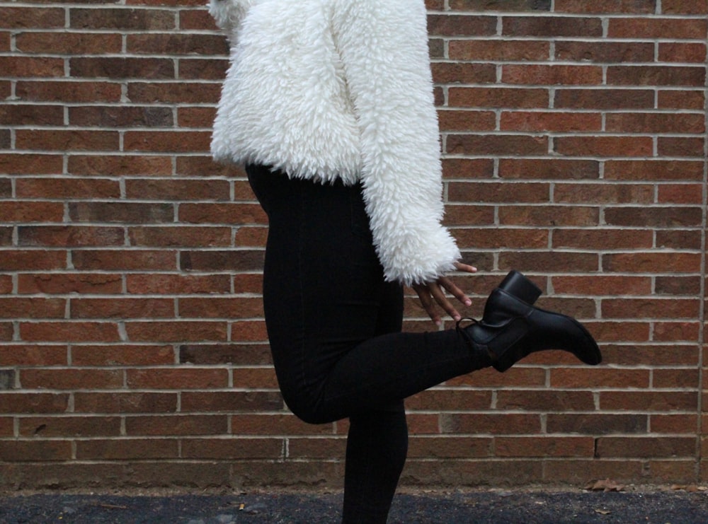 woman raising her left foot near brown brick wall during daytime