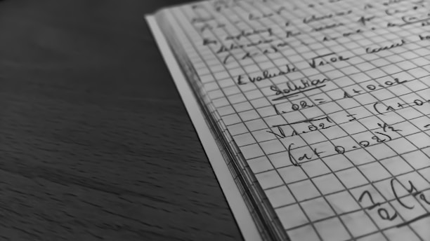 A close-up view of an open notebook with graph paper containing handwritten mathematical notes and equations. The notebook rests on a wooden surface with a focus on the neatly aligned lines and clear, precise writing. The overall scene is presented in black and white, giving a classic and studious appearance.