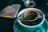 closeup photo of green ceramic cup with tea pouring through a metal strainer