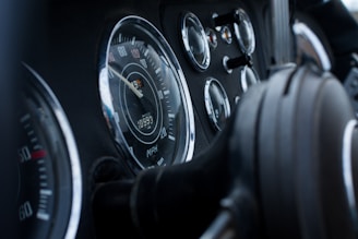 A close-up view of a vehicle dashboard featuring various gauges including a speedometer, odometer, and other dials. The design is classic with chrome edges and a focus on the speedometer in the center.