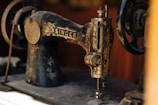 A vintage sewing machine with ornate floral designs and the brand label is prominently displayed. The metal parts show signs of age and wear, contributing to its antique aesthetic.