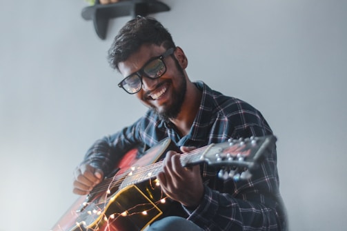 An adult student smiling while strumming guitar strings in a home setting.