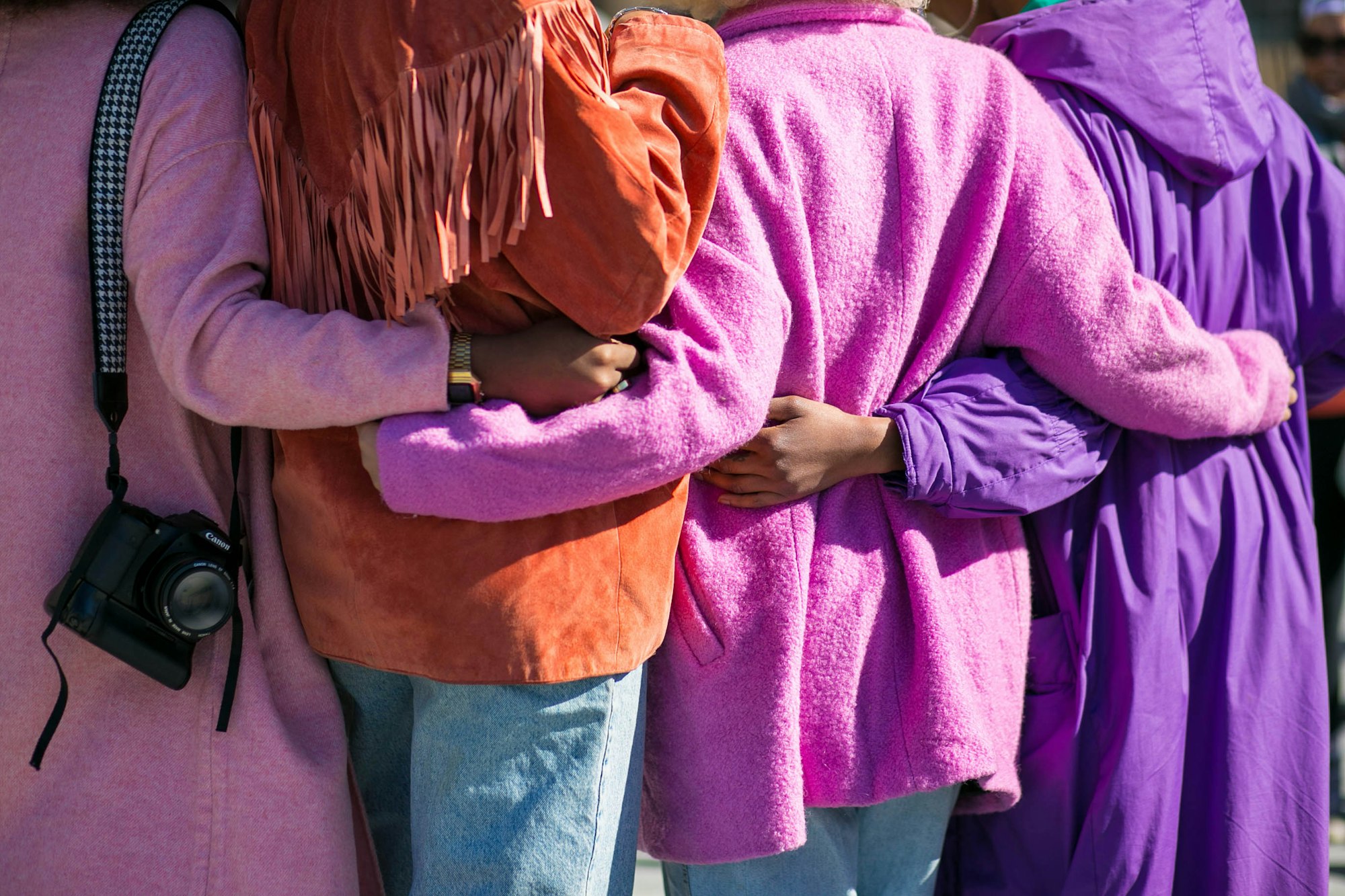 Women in hugging in a line wearing pink and purple for International Women's Day.