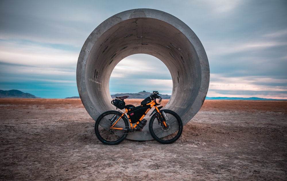 Bicicleta preta e laranja na areia marrom perto do mar durante o dia