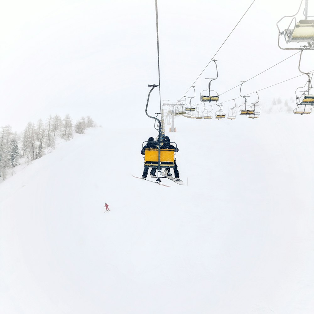 two person riding on cable transportation through top of the hill during winter