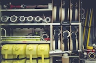 A neatly organized collection of firefighting equipment, including coiled hoses, metal nozzles, yellow plastic containers, and various metal pipes and fittings. The equipment is stored within compartments on a fire truck, showcasing its readiness and accessibility.