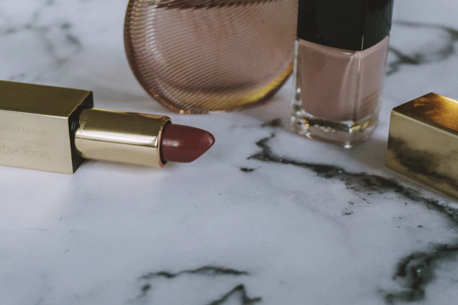 Close-up of a sleek Auruméa lipstick with gold accents on a cream marble surface.