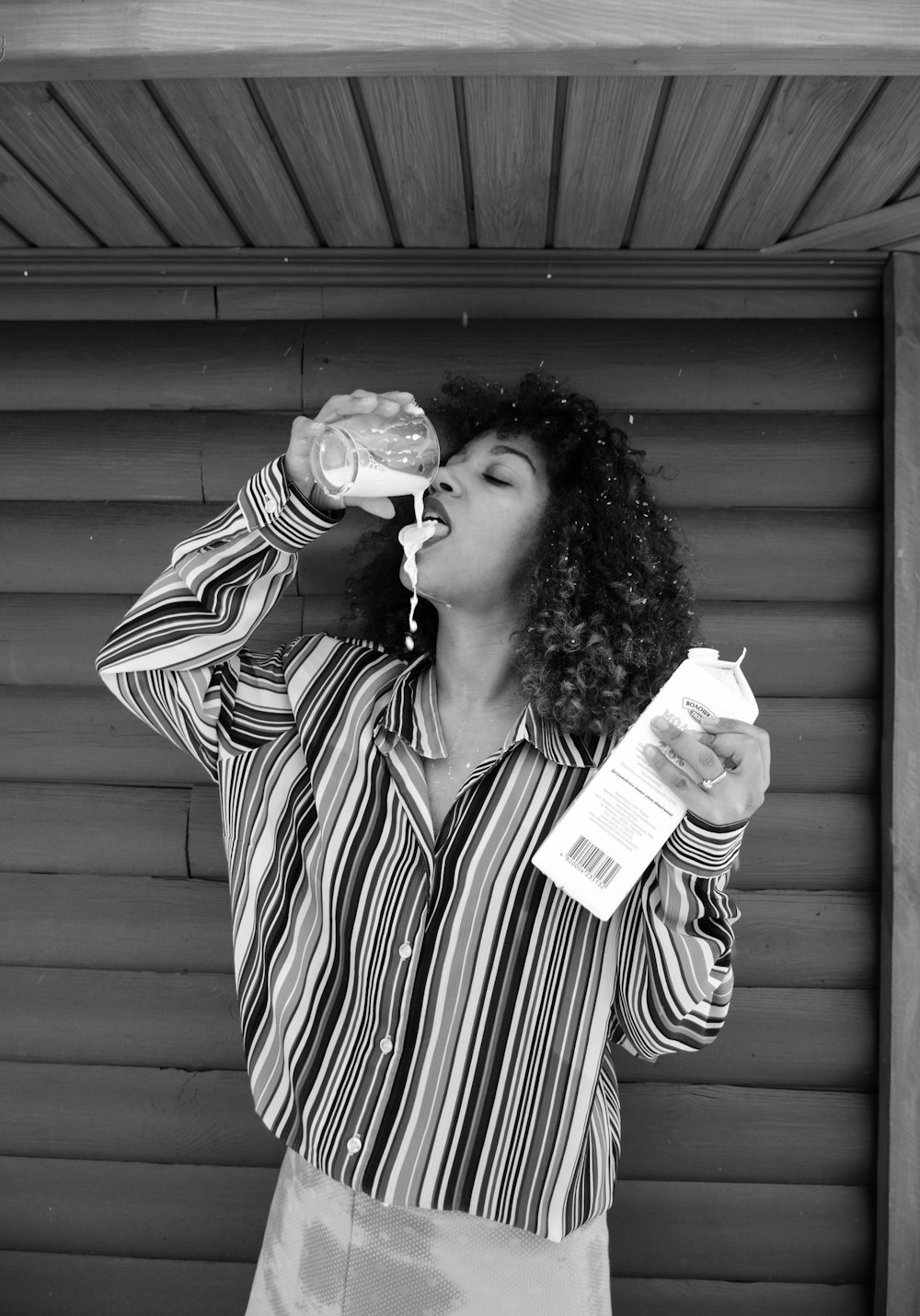 greyscale photo of woman drinking milk near wood wall panel