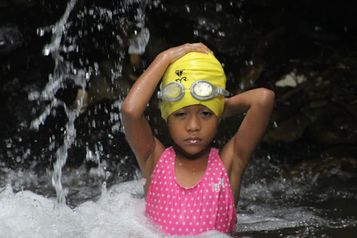A cheerful young child in bright swim gear happily learning to float in a calm pool, with a friendly swim instructor guiding nearby.