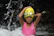 A joyful young child in a bright swim cap splashing happily in a clear indoor pool.