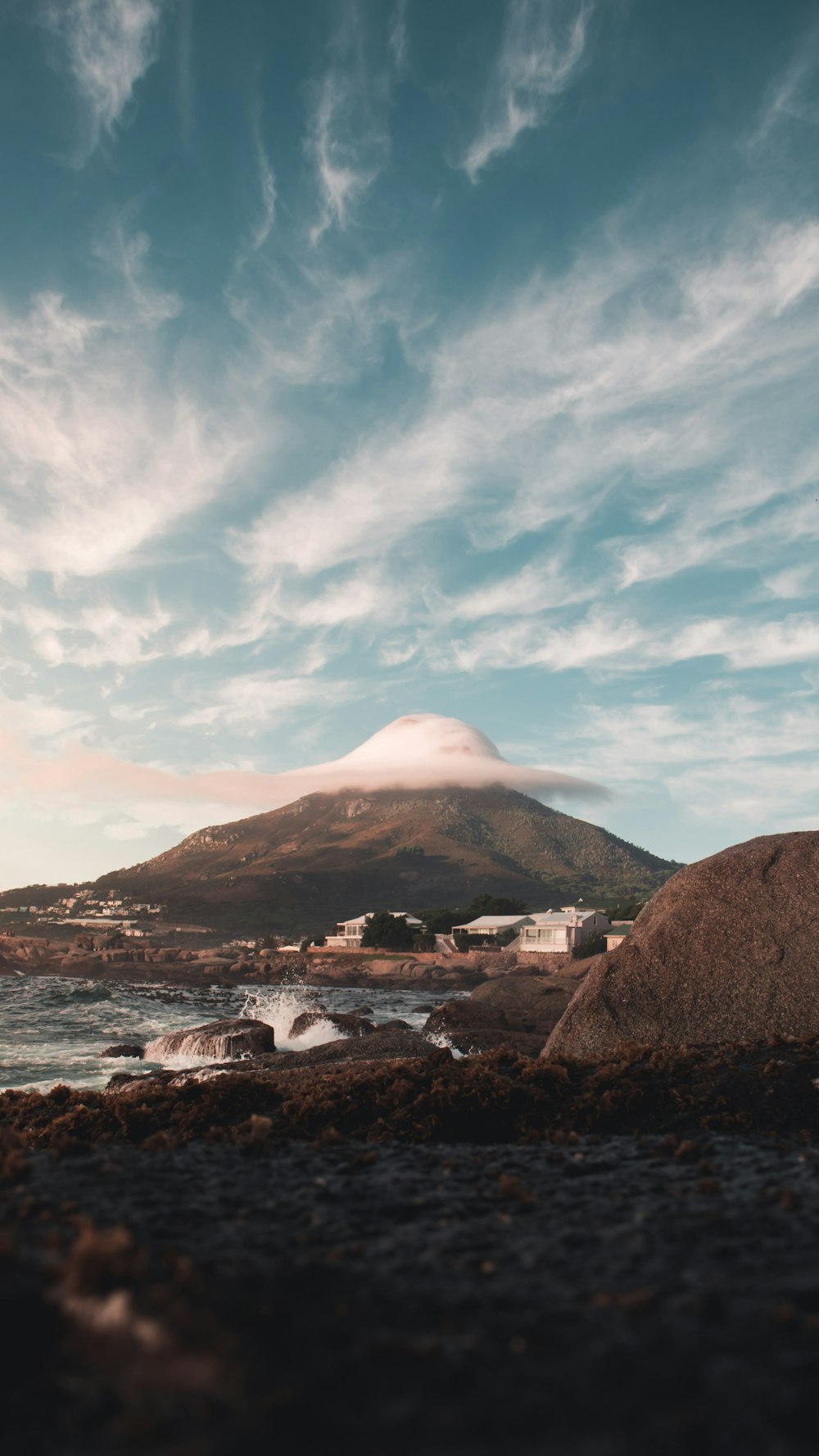 brown rocky mountain beside body of water covered with clouds during daytime