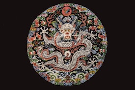 A detailed and vibrant embroidery showcases a mythical dragon surrounded by intricate floral and cloud motifs. The dragon is centrally featured with a fierce expression, and its scaled body winds through the circular design. The elaborate use of colors and textures lends an ornate and traditional feel.