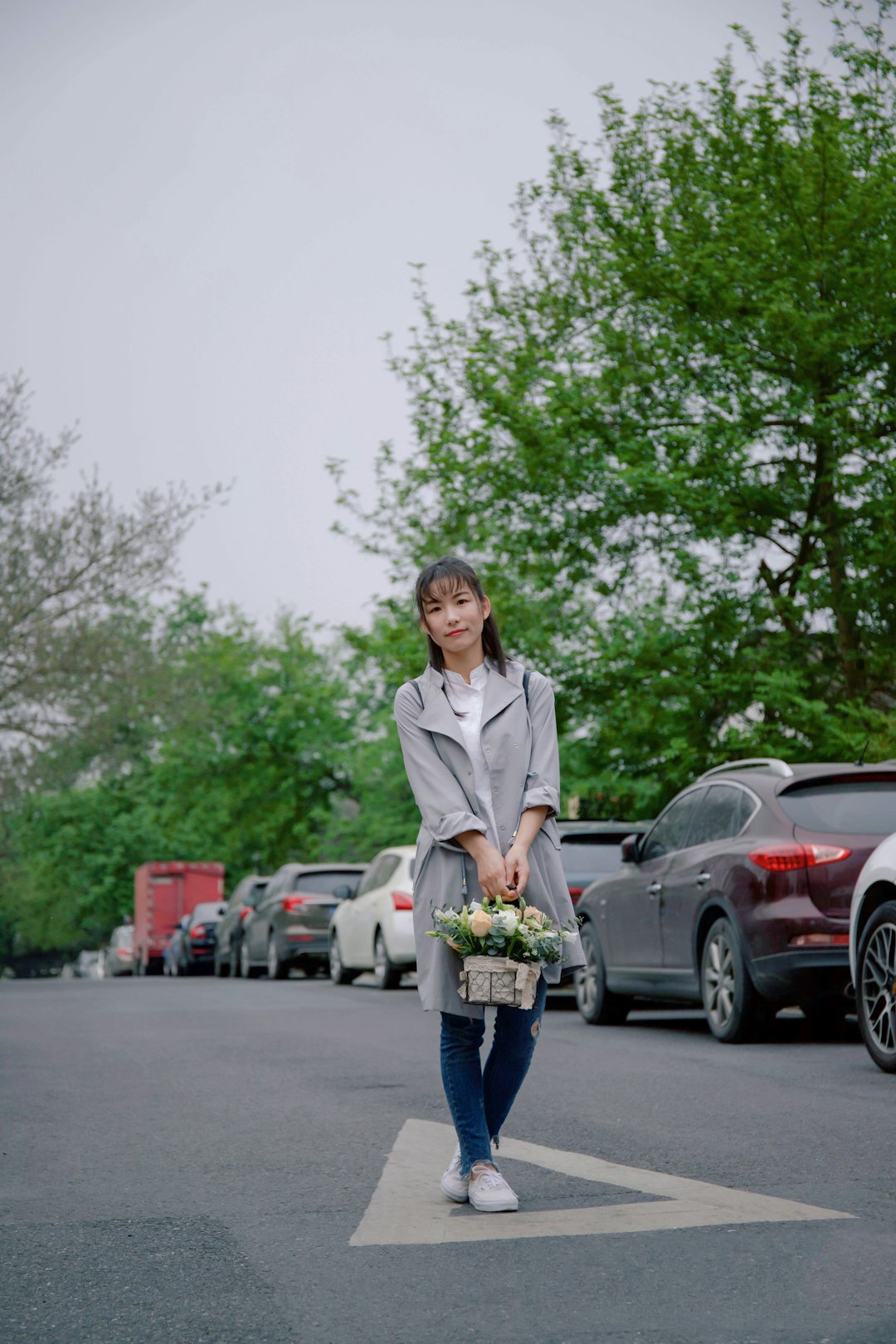 woman holding basket of flower standing in middle of road near parked vehicles