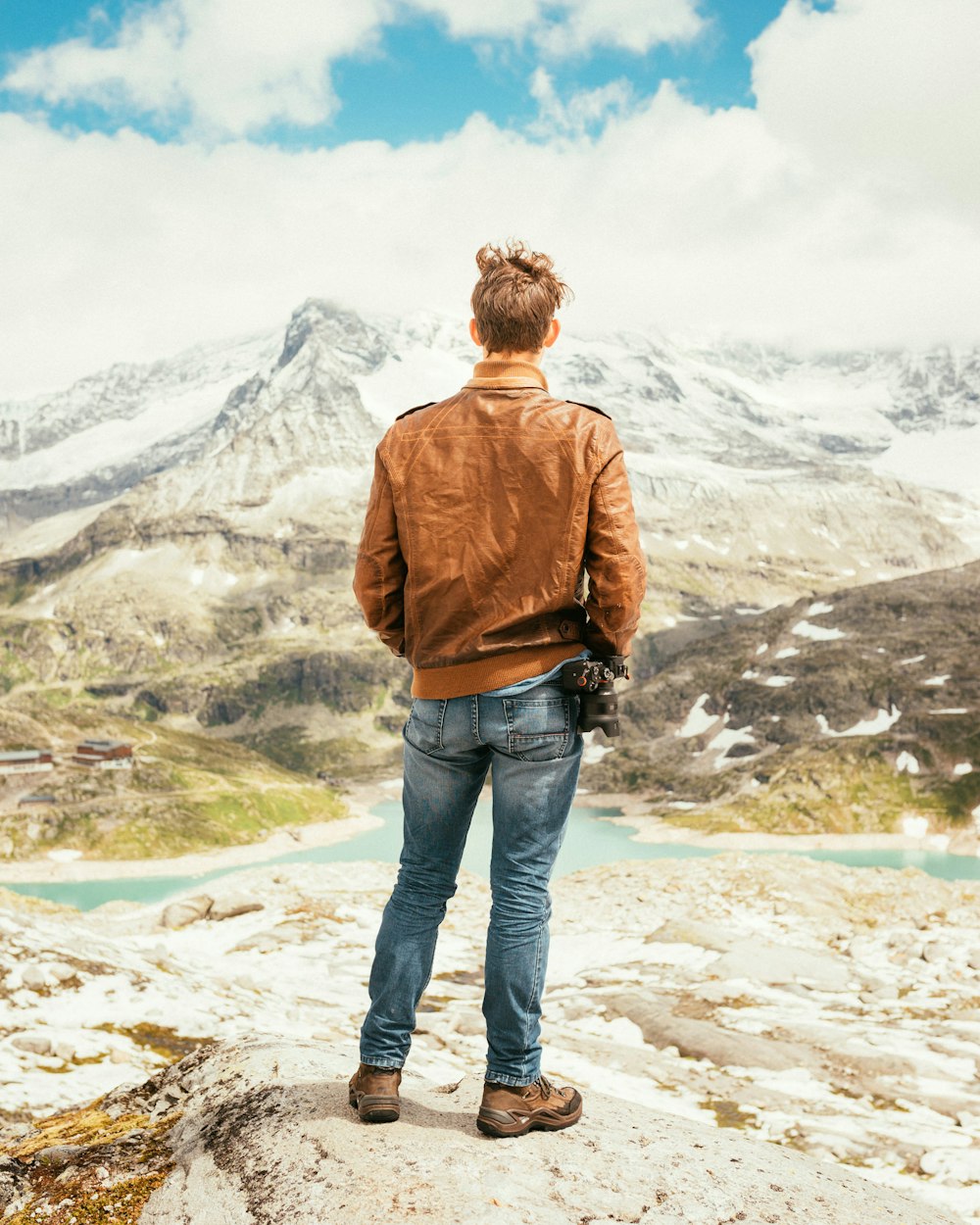 Uomo in piedi sulla roccia di fronte al lago e alle montagne durante il giorno