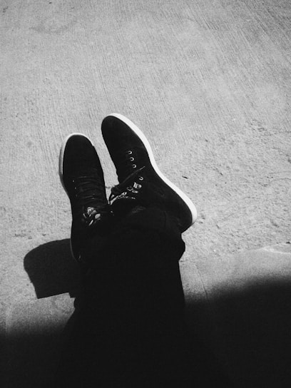 grayscale photography of person wearing black sneakers sitting on floor