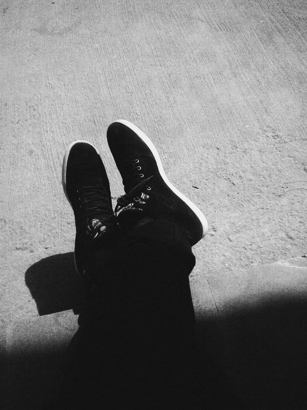 grayscale photography of person wearing black sneakers sitting on floor