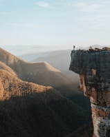 man standing on rock cliff overlooking mountains