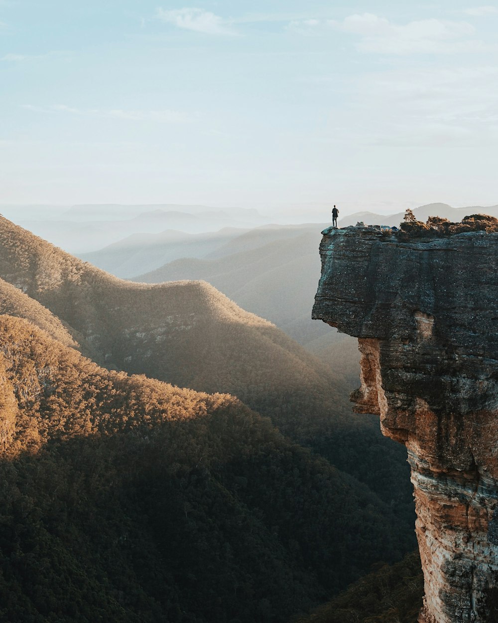 man standing on rock cliff overlooking mountains