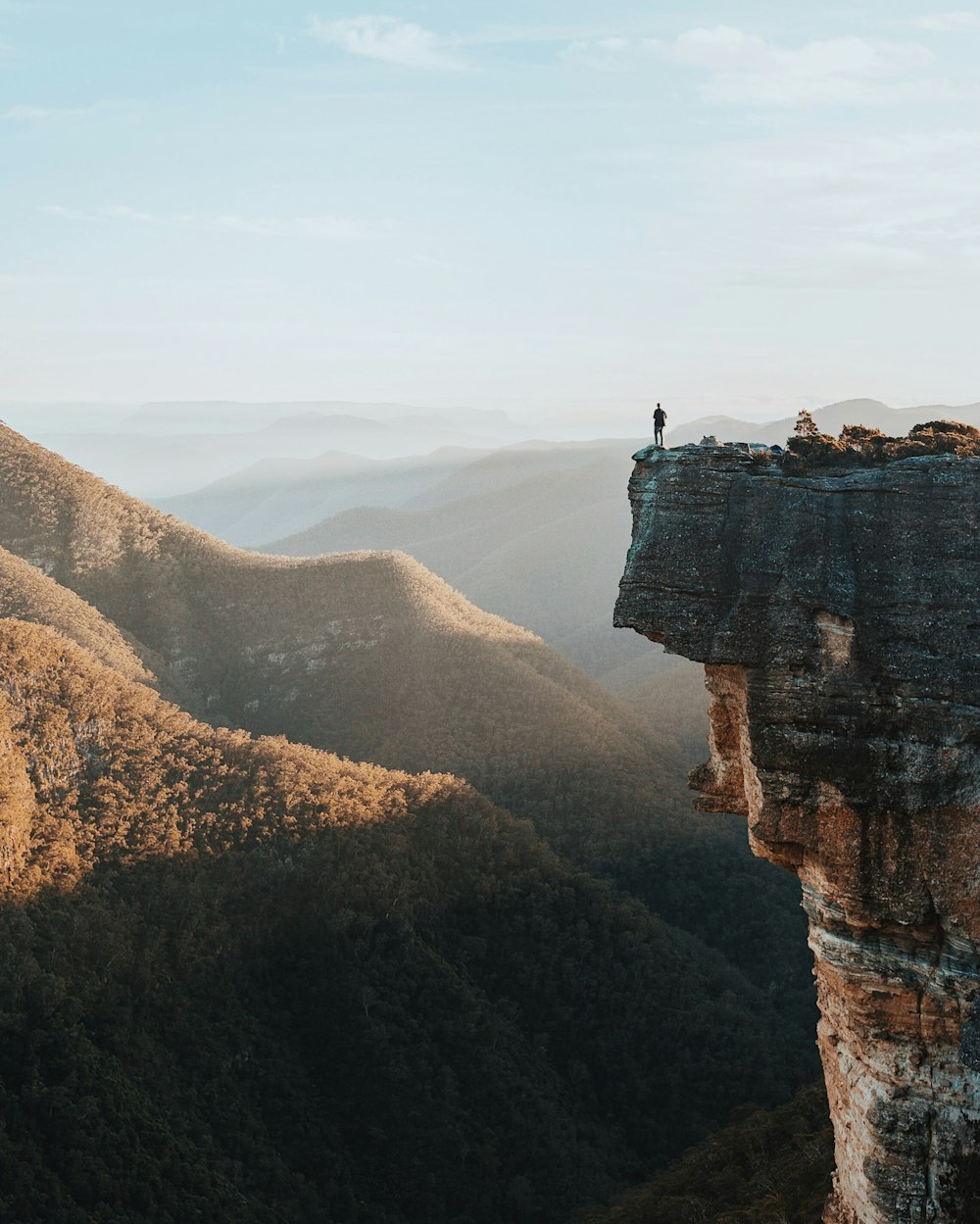 hombre de pie en el acantilado de roca con vistas a las montañas