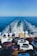 A ferry is transporting multiple parked cars across a vast expanse of blue ocean under a clear sky. The rear of the ferry shows the wake trailing behind, and numerous vehicles are tightly arranged on the ferry's deck.
