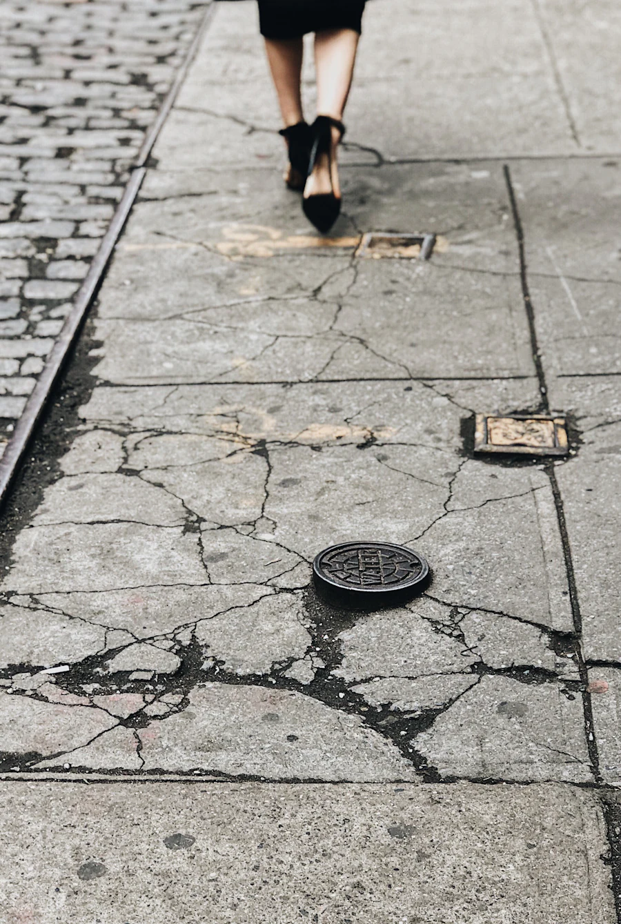 Cracked New York City sidewalk surrounding metal utility covers and pavement hardware