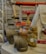 A collection of plumbing fittings and components is arranged on a surface. Notable items include a brass valve with a red handle, a couple of elbow joints, and a rolled-up white hose. In the background, a red and black ladder can be seen along with some metal poles against a concrete wall.
